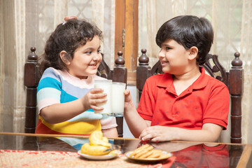 Happy little Indian kids drink milk having breakfast in kitchen, healthy lifestyle, Protein and calcium