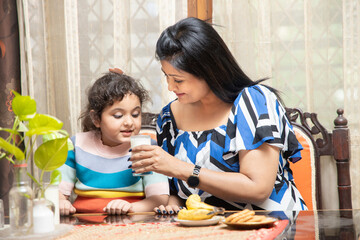 Obraz na płótnie Canvas happy Indian asian family mother and cute little daughter drink milk having breakfast in kitchen, healthy diet, protein and calcium