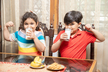 Happy little Indian kids drink milk having breakfast in kitchen, healthy lifestyle, Protein and...