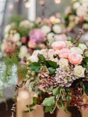 Wedding bouquet in gentle tones of white and pink roses, dry hydrangea, barberry twigs, and green leaves. In the background is a flower decoration.