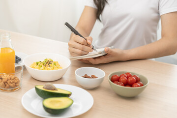 Diet, Dieting hand of asian young woman, girl write diet plan nutrition on table is different food ingredients in the green. Nutritionist of healthy, nutrition of weight loss, health care people.