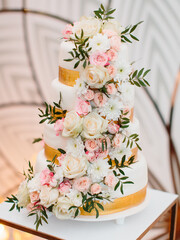 Four-tiered white wedding cake with gold ribbons, decorated with white and pink roses, chrysanthemums, and leaves.