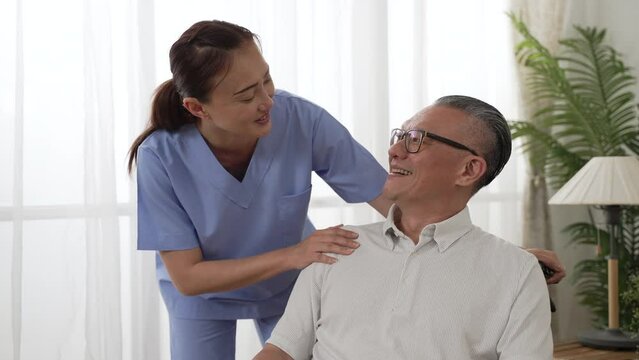 Slow motion with closeup of smiling Asian female resident care attendant giving mental support and words of encouragement to the mature man patient at home