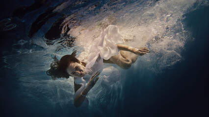 Fototapeta na wymiar A girl with long dark hair swims underwater as if flying