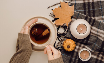 Hands with cup of tea with cinnamon and anise, autumn decorations and candles. Top view hands with tea, flat lay, autumn concept