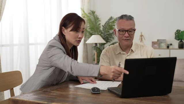 asian female insurance agent showing information on computer and answering the senior customer&rsquo;s questions while they are discussing long-term care plans at home