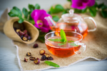 brewed rosehip tea in a glass teapot with rosehip flowers and mint
