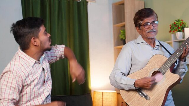 Happy father with son dancing by playing guitar at home - concept of leisure retirement lifestyles, family bonding and freedom