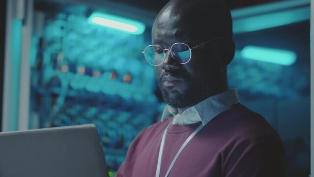 Tilt up shot of African American IT professional working on laptop in server room of data center