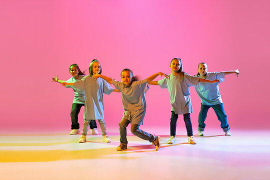 Group of children, little girls in sportive casual style clothes dancing in choreography class isolated on orange background in purple neon light.