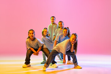 Portrait of cheerful, active little girls, happy kids dancing isolated on orange background in neon...