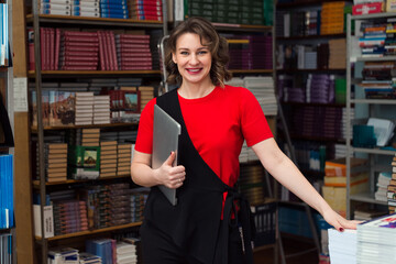 professional woman educator or manager posing at public library of high school or college, holding...