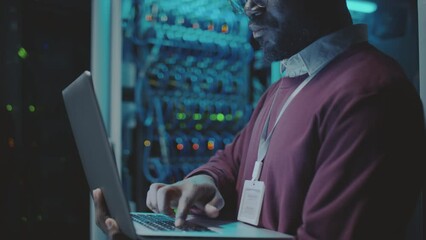 Cropped shot of African American system administrator standing in server room and using laptop while working in data center