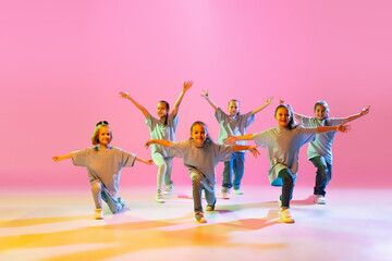Portrait of cheerful, active little girls, happy kids dancing isolated on orange background in neon...