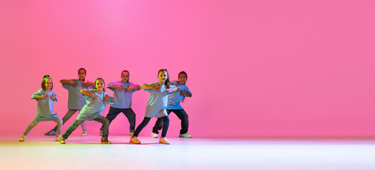 Hip-hop dance, street style. Happy children, little active girls in casual style clothes dancing isolated on orange background in purple neon light.