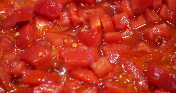 Pieces of tomatoes are fried in a pan.