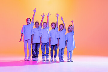 Dance group of happy, active little girls in t-shirts and jeans in action isolated on orange...