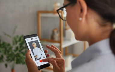 Finding love. Woman who is looking for love scrolls through profiles of men in dating application on mobile phone. Close up of woman presses red heart button to like man who appeared on screen.