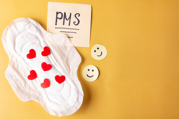 Women's Menstrual pads (sanitary napkin) with red hearts, PMS inscription and funny emoticons on a yellow background. Women's health in critical days. Space for text.