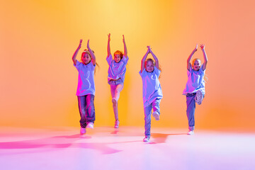 Dance group of happy, active little girls in t-shirts and jeans in action isolated on orange...