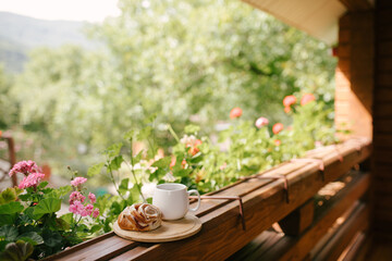 Mug with tea and cinnabon on tray on cozy balcony of wooden cottage.