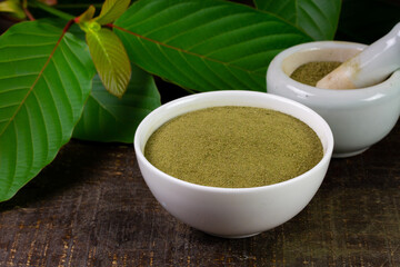 Mitragyna Speciosa Korth or kratom powder on white bowl with white mortar and pestle and green leaf...