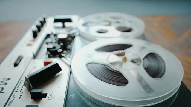 An old reel-to-reel tape recorder plays music by scanning a magnetic tape.