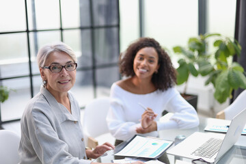 Two business women smile while working together on a laptop at a table in the boardroom in the office