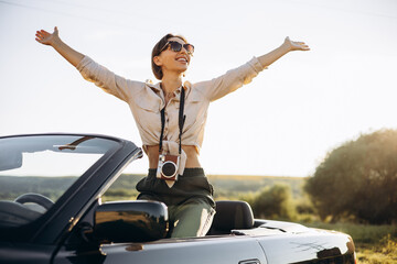 Woman standing in car cabriolet with camera on her neck