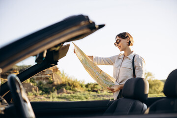 Woman road tripping by cabriolet and looking at the map