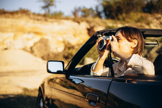 Woman road tripping by cabriolet and making photos on camera