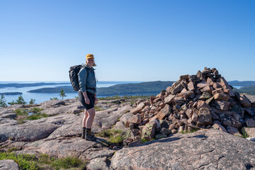 Obraz premium Caucasian outdoor active young adult woman at Mountain Summit in Skuleskogen National Park Sweden, with outdoor hiking clothes and cap smiling and looking at camera with Horizon Scenery in Background.