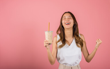 Excited Asian beautiful woman holding drinking brown sugar flavored tapioca pearl bubble milk tea, Happy smiling portrait female success, isolated on pink background, pearl milk tea beverage concept