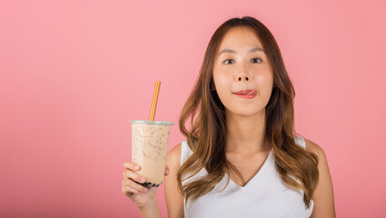 Asian woman holding drinking brown sugar flavored tapioca pearl bubble milk tea lick lips wanna taste have delighted summer holiday dream, smile female, isolated on pink background, beverage concept
