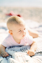 Baby lies with his fists clenched on his tummy on a blanket