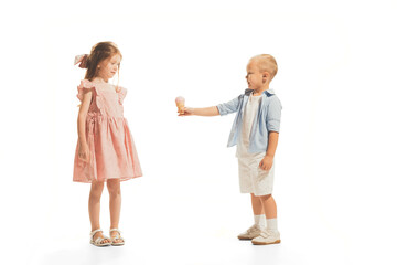 Portrait of children, little boy giving ice cream to beautiful girl isolated over white studio background