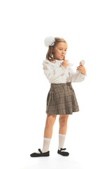 Portrait of little girl, child in school uniform with bows applying lipstick, playing isolated over white studio background