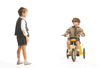 Portrait of children, boys in vintage outfits playing together, having fun, riding small bike...
