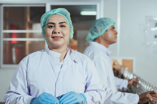 Senior female employee worker in uniform working clean and check for dirt glass bottles for juice drinks in beverage factory industry