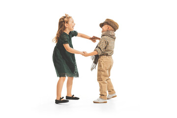 Portrait of children, boy and girl in vintage clothes playing together, having fun, posing isolated over white studio background
