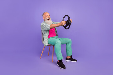 Full length profile photo of excited handsome person hold wheel sit chair look copyspace isolated on violet color background