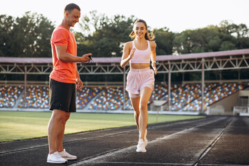 Woman running on stadium with trainer using stopwatch