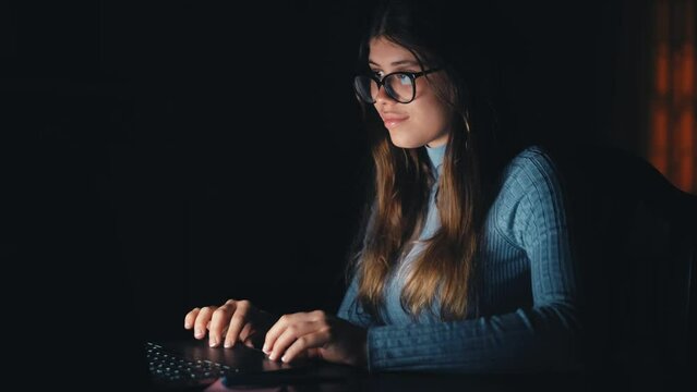 One beautiful and young woman using computer working at late night at home. Caucasian teenager wearing eye glasses studying for a test.