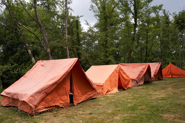 Side view of a group of orange tents by the river at a children's summer camp. Many tents in a wild area in the forest.