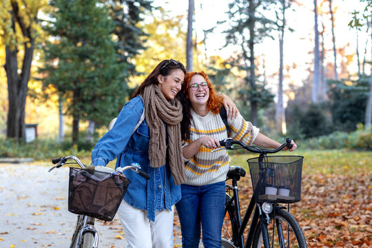 Two woman push bikes and talk funny stories and smile in public park