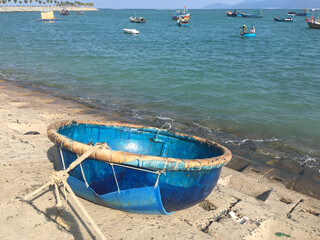 Vietnamese traditional round woven bamboo boat on sandy shore. Seascape with wooden fishing boats