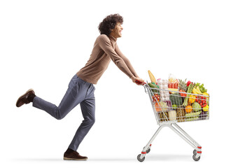 Full length profile shot of a young man running with a shopping cart
