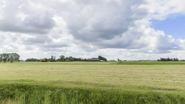 Moving clouds over a farm with horses grazing in a field - time lapse