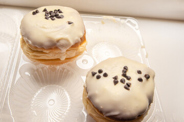 Two delicious donuts with icing sugar and chocolate chips on a white background in a transparent plastic container