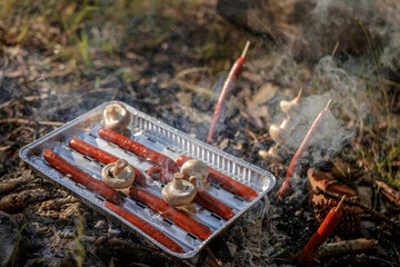 Obraz premium Grilling sausages and mushrooms on campfire..The concept of adventure, travel, tourism, camping, survival and evacuation.